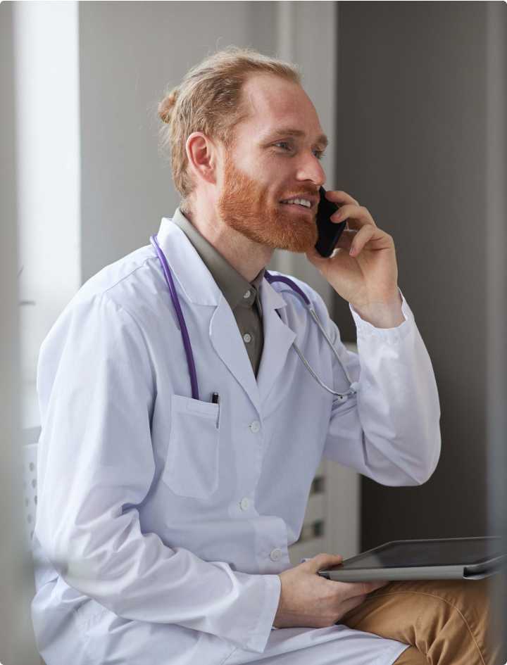 Doctor who is taking a call on his mobile phone while holding a tablet computer.