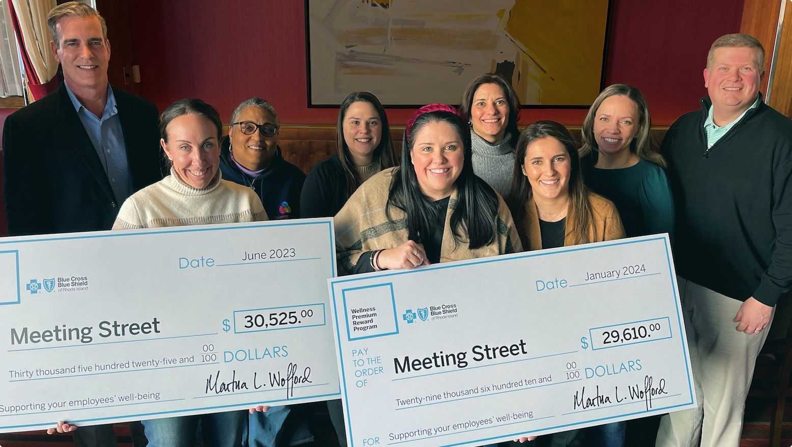 Smiling employer group holding oversized checks.